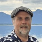 Frank Seipel Sprecher des Grünen Ortsverbands Prien, steht vor dem Chiemsee. Blickt freundlich in die Kamera.