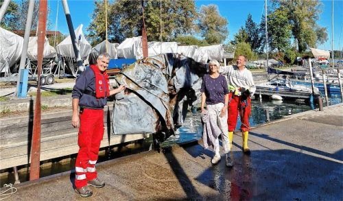 Drei Personen am Hafen mit geborgenem Schrottteil, vermutlich aus dem Wasser gezogen, bei einer Umweltaktion.